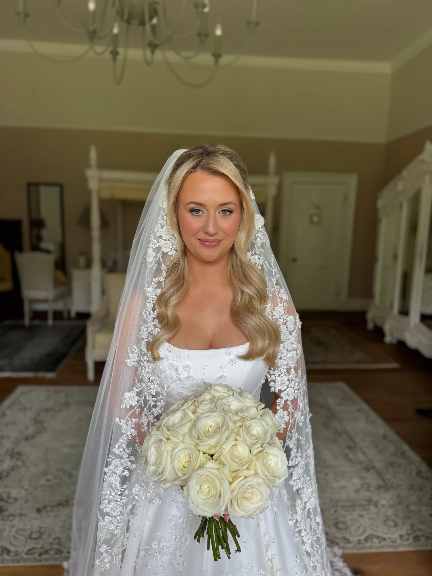 Smiling blonde bride with soft waves under a long lace-edged veil